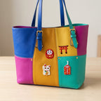 daruma doll torii gate maneki neko and omamori embroidered patches on a blue yellow and teal leather bag