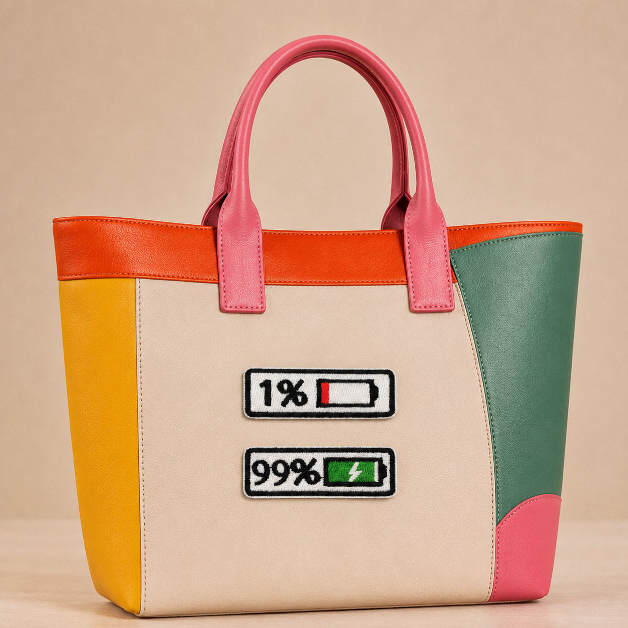 two battery status embroidered patches showing 1% and 99% on a bold color-block leather tote bag