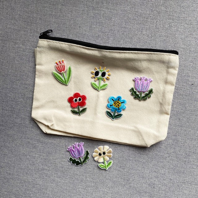 assorted googly eyes floral embroidered patches on a natural canvas pouch