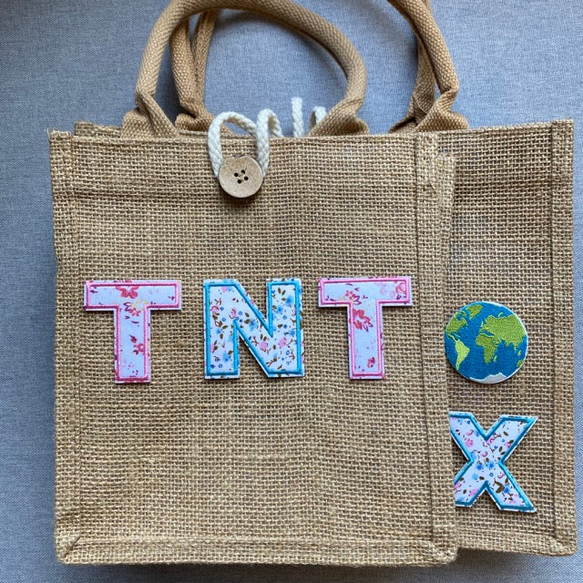 floral alphabet embroidered patches spelling TNT with earth and X patches on a burlap tote bag