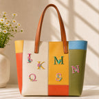 flower and alphabet patches J K Q M S N on a bold orange yellow and green color-block leather tote bag