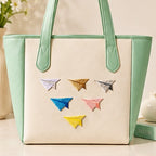cute paper airplane embroidered stick-on patches on canvas tote bag — six colourful paper airplane patches arranged in a flock formation