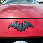 large black faux leather bat stick-on patch on a red car hood