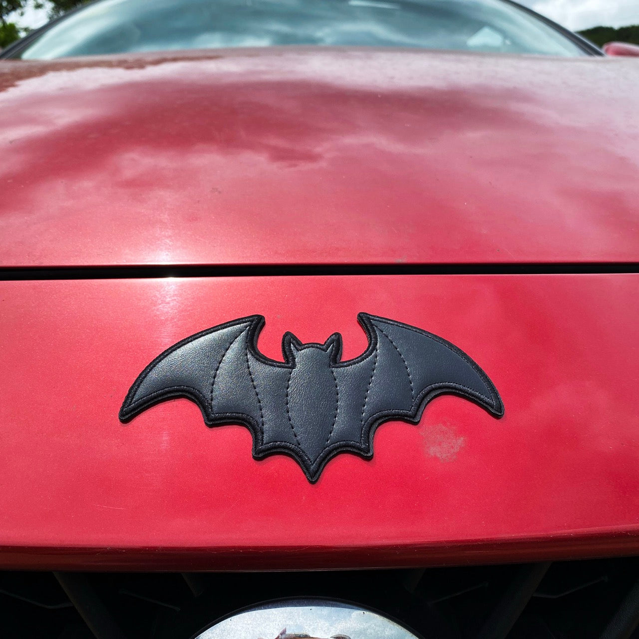 large black faux leather bat stick-on patch on a red car hood
