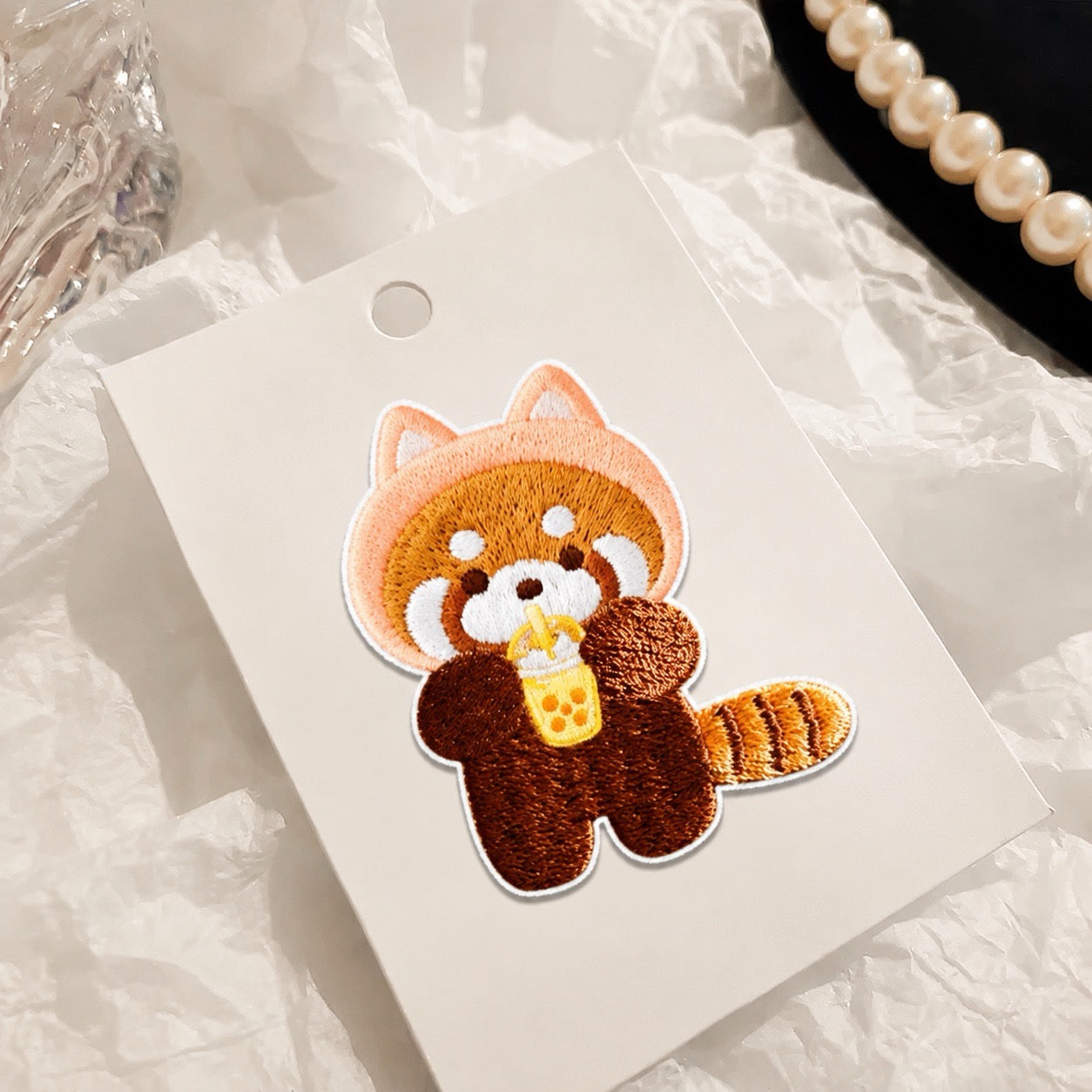 red panda drinking boba tea embroidered stick-on patch on display card — warm tones with pearl and glass styling
