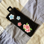Black zippered pouch decorated with blue and pink blossom patches and a leafy floral cluster
