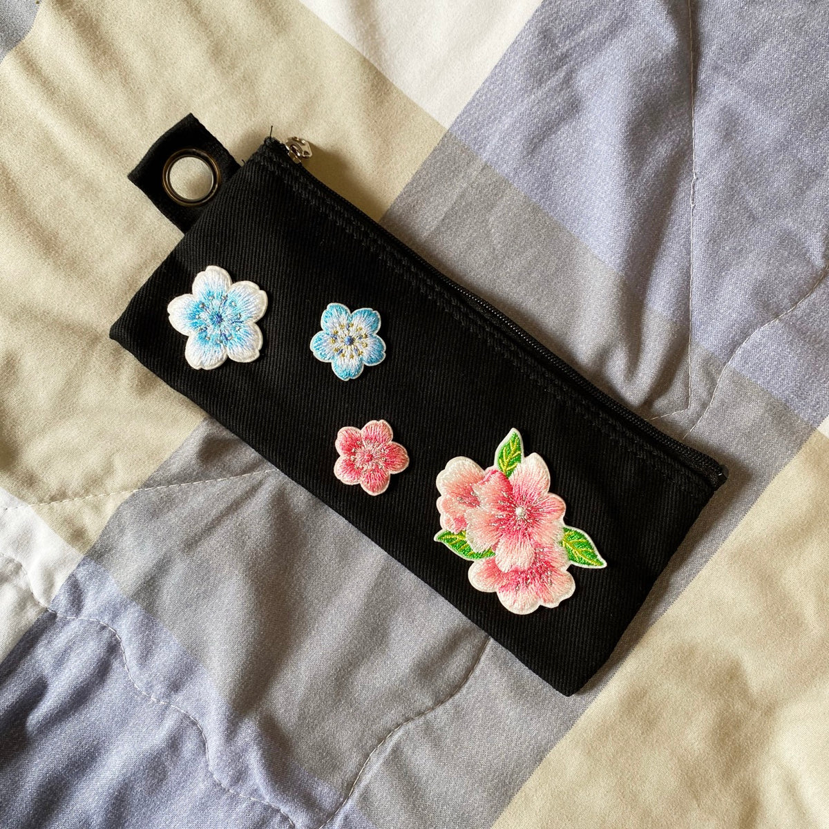 Black zippered pouch decorated with blue and pink blossom patches and a leafy double bloom

