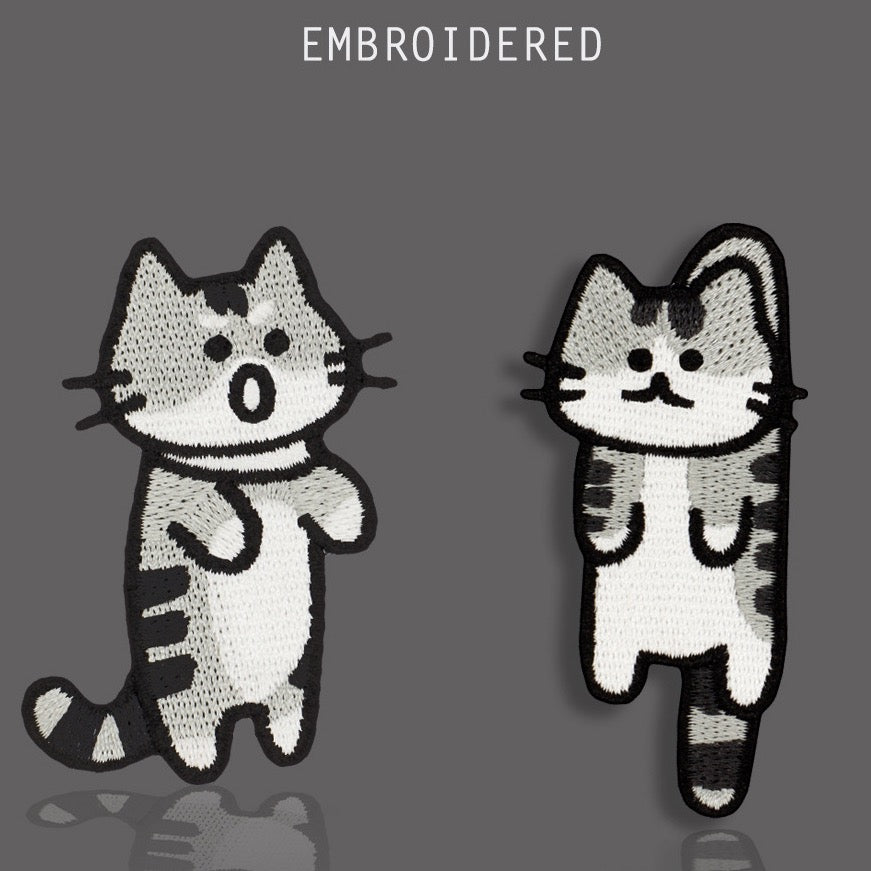 Two funny gray tabby cat embroidered stick-on patches with contrasting expressions
