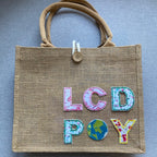 floral letter embroidered patches spelling LCD POY on a burlap tote bag