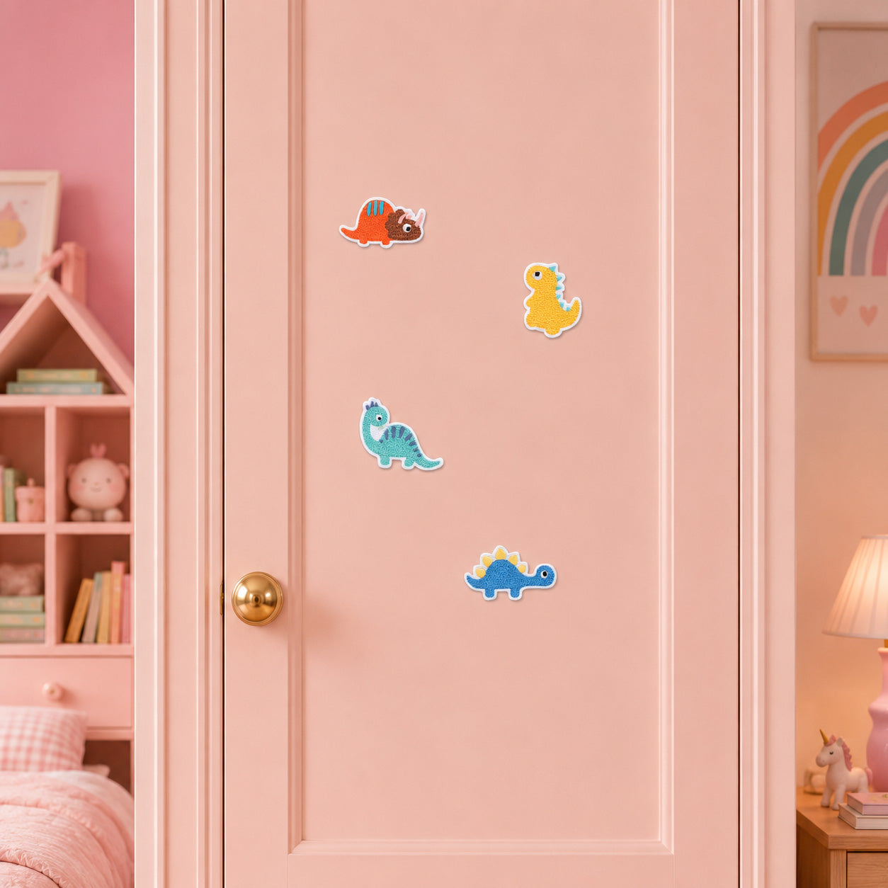 four cute cartoon dinosaur embroidered patches with triceratops t-rex brachiosaurus and stegosaurus stuck on a pink wardrobe door in a girls room
