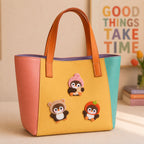 cute penguin in bear and strawberry costume stick-on patches decorating a yellow and pink color-block leather handbag