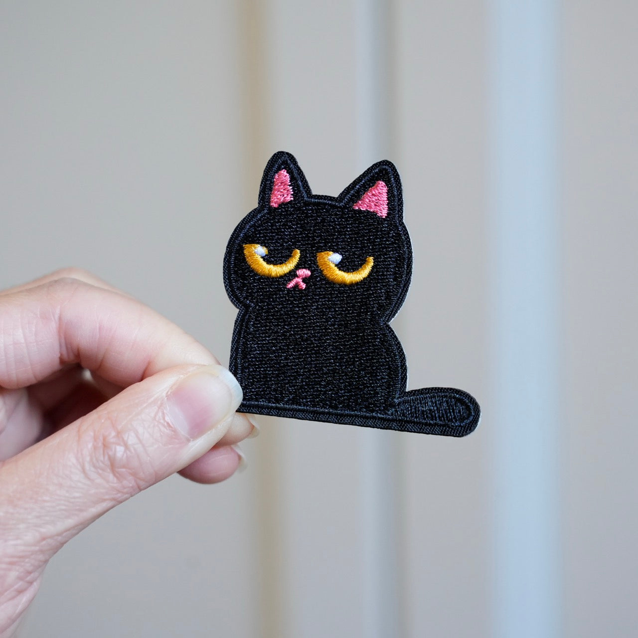 holding a big-eyed cat embroidered stick-on patch in hand