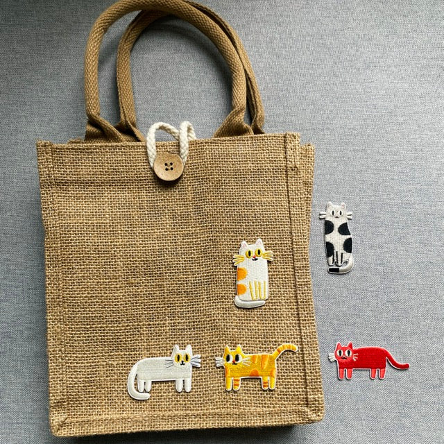 funny derpy cat embroidered patches on a burlap tote bag with loose patches beside it