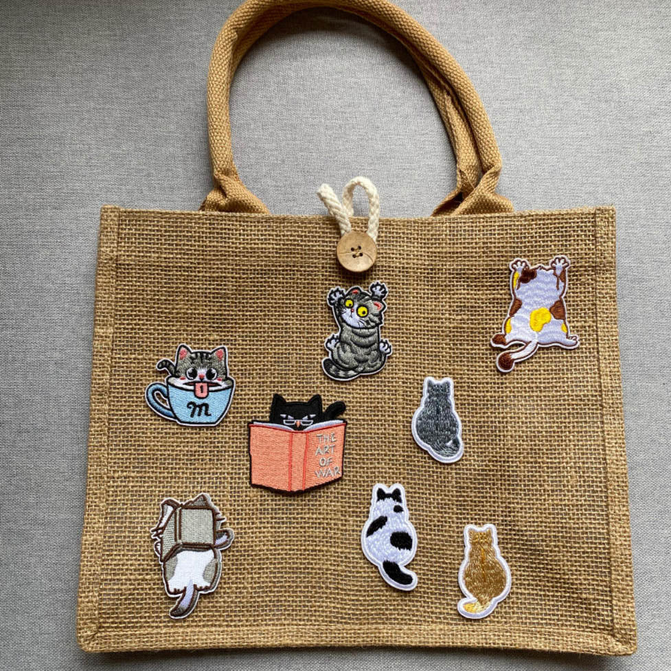 chubby cat embroidered stick-on patches in various poses on a natural jute tote bag
