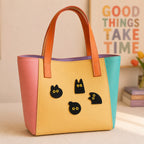 cute black cat with yellow eyes stick-on patches decorating a pink and yellow color-block leather handbag