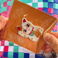 animated peel and stick demo of lucky beckoning cat maneki neko embroidered patch applied to a woven bag