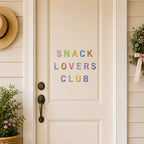 minimalist alphabet stick-on patches spelling snack lovers club in pastel rainbow colors on a white front door with wreath