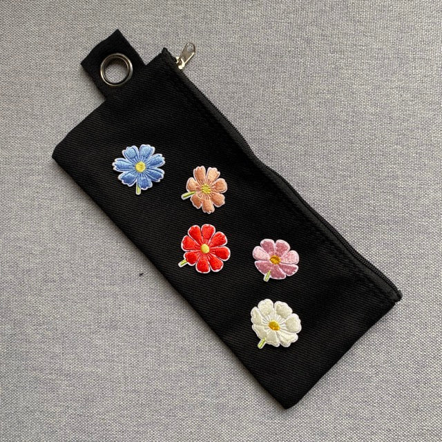 five cosmos flower embroidered patches in different colors on a black denim pencil case