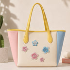 Pastel tote with yellow handles decorated with pink and blue cherry blossom embroidered patches
