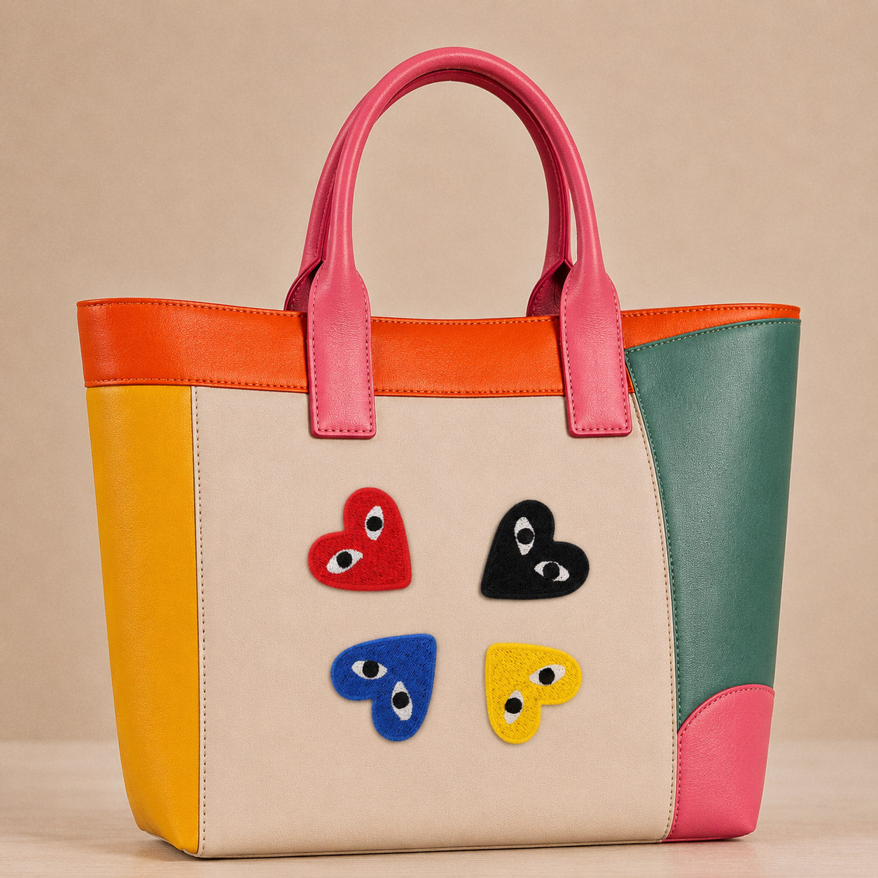 red black blue and yellow heart with eyes stick-on patches decorating a pink and orange color-block leather handbag