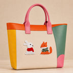 white bunny in red scarf and orange fox in green polka dot scarf stick-on patches decorating a pink and orange color-block leather handbag