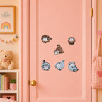 chubby round pallas cat with leopard markings and blue cat with pink blush in curled rolling and lying poses stick-on patches on a pink door in a pastel room