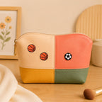 sports ball soccer and basketball embroidered patches on a four-color colorblock cosmetic pouch in cream coral yellow and olive green with gold zipper