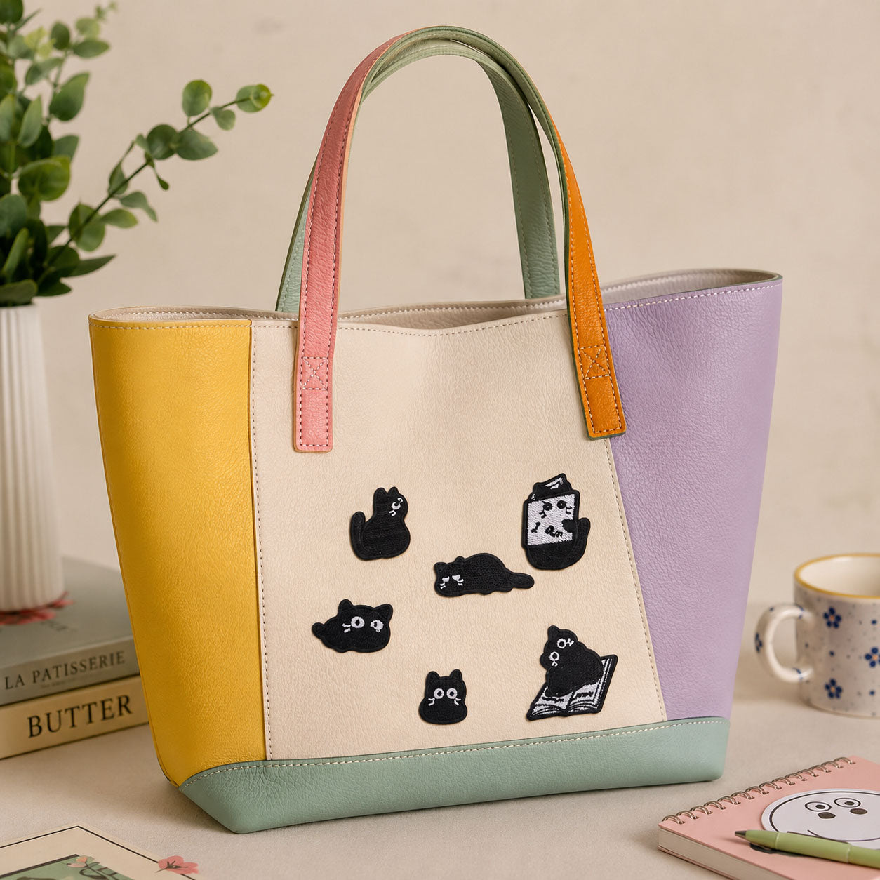 black void cat in various lazy poses including reading a book stick-on patches decorating a yellow and purple color-block leather handbag