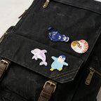 anglerfish, nautilus, dolphin, and penguin embroidered patches on a black waxed canvas backpack