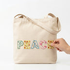floral letter embroidered patches spelling PEACE being applied to a natural canvas tote bag