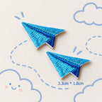 blue paper airplane embroidered stick-on patches — pair of bright blue satin embroidery paper planes with deep blue fold crease detail 33x18mm