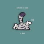 cat tail and legs embroidered stick-on patch — grey tabby back half with striped body curved tail and dangling white paws going over an edge