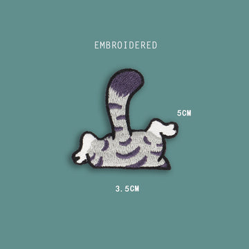 cat tail and legs embroidered stick-on patch — grey tabby back half with striped body curved tail and dangling white paws going over an edge
