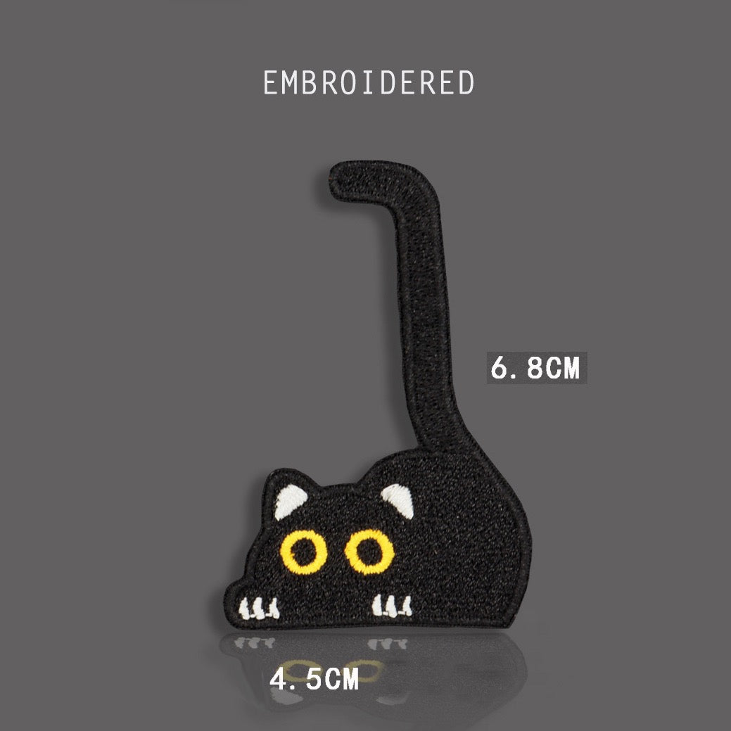 tall tail peeking black cat embroidered stick-on patch — crouched black cat with tail shooting straight up large yellow eyes and white paw detail