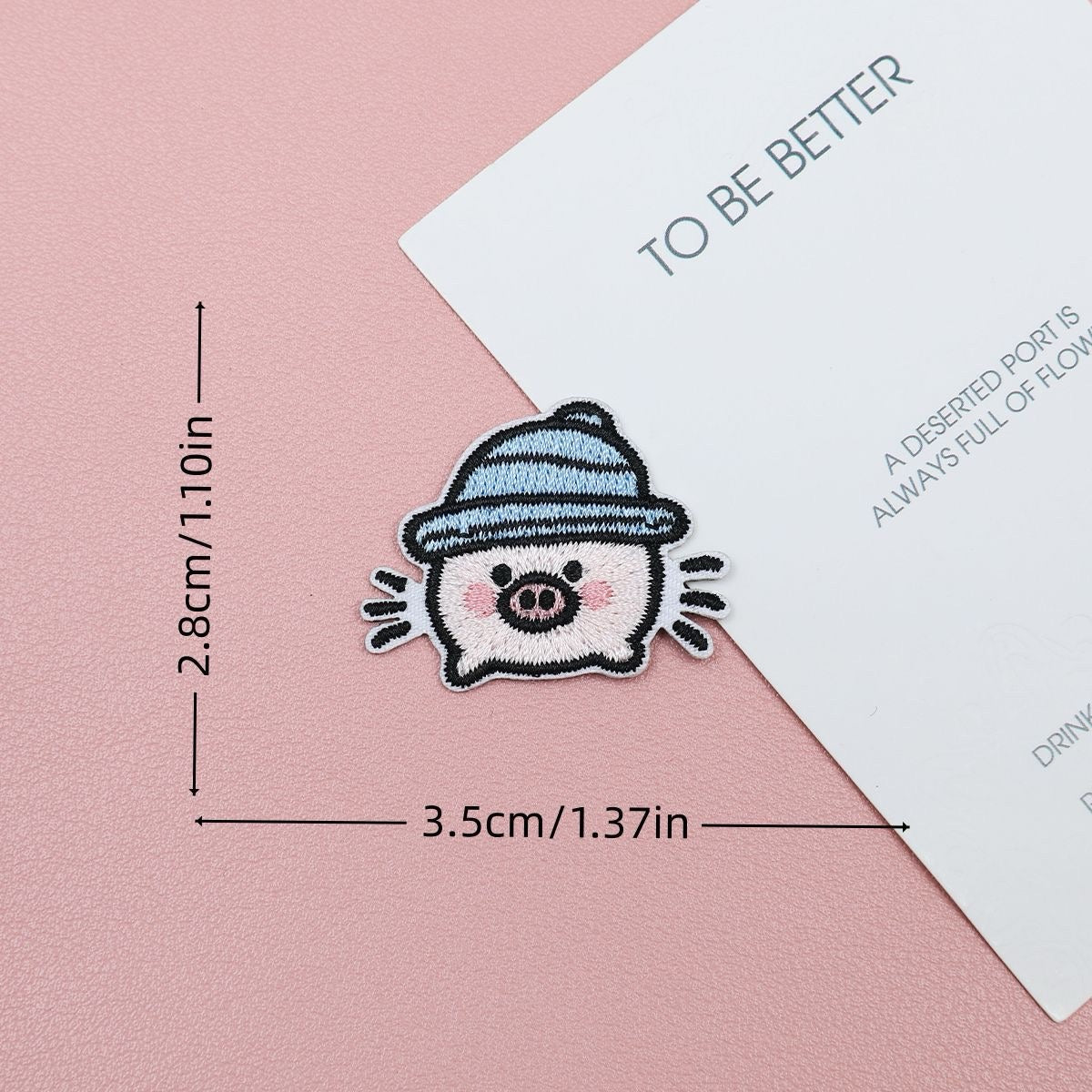 Pink piglet embroidered stick-on patch wearing a blue striped hat with playful motion lines
