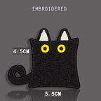square sitting black cat embroidered stick-on patch — blocky square black cat with white triangular ear tips curled tail and large yellow eyes looking outward
