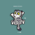 climbing front cat embroidered stick-on patch — grey tabby face-on with large yellow eyes white chest and four splayed paws mid-climb