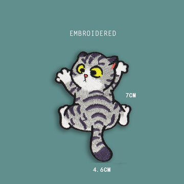 climbing front cat embroidered stick-on patch — grey tabby face-on with large yellow eyes white chest and four splayed paws mid-climb