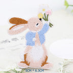 Seated bunny embroidered patch in a blue jacket holding white, yellow, and pink flowers
