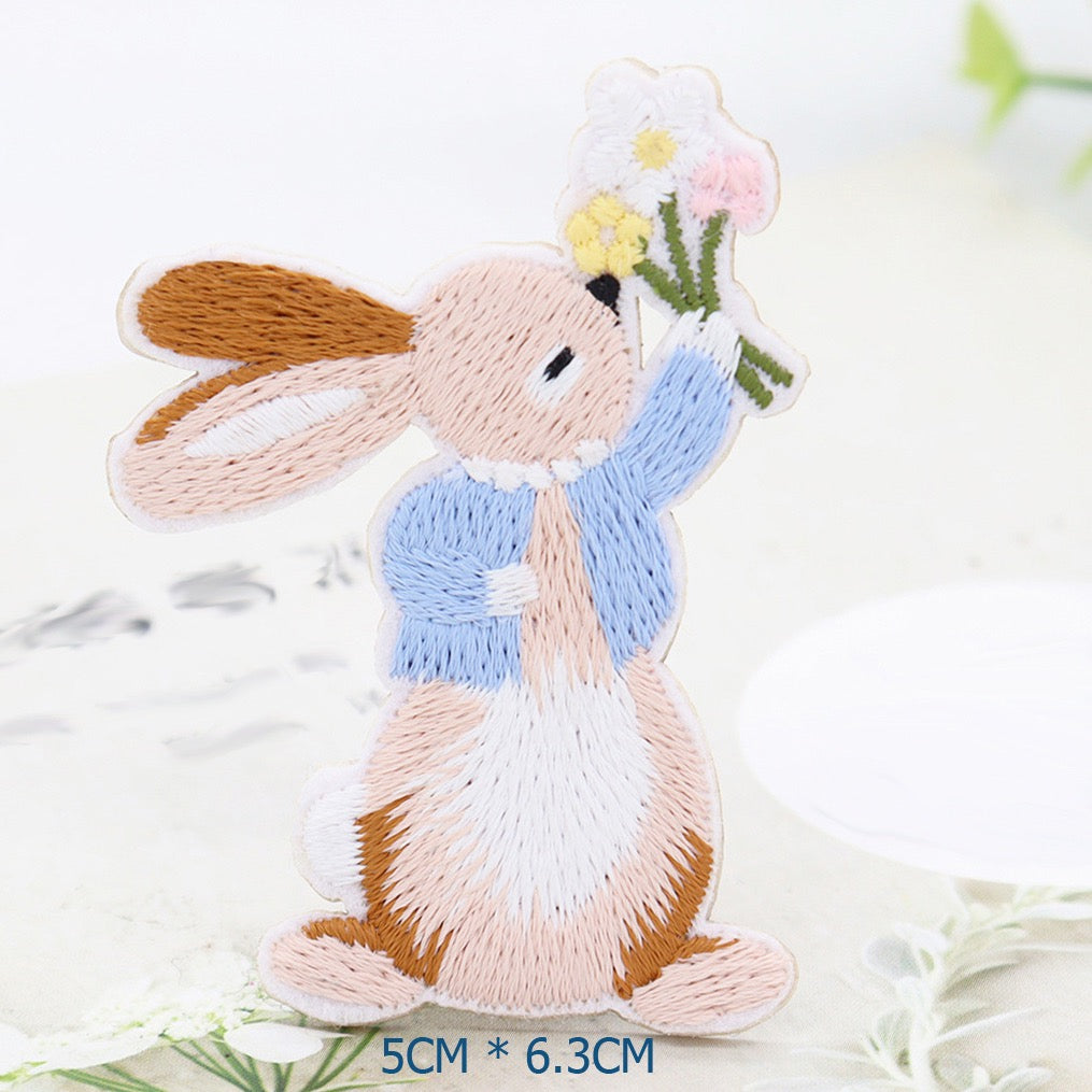 Seated bunny embroidered patch in a blue jacket holding white, yellow, and pink flowers
