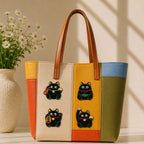 black maneki neko cat holding fish coin ingot and lucky charm stick-on patches decorating a bold orange yellow and olive stripe leather handbag