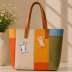 calico and tabby cat in funny arms-out dancing pose stick-on patches decorating a bold orange yellow and olive stripe leather handbag