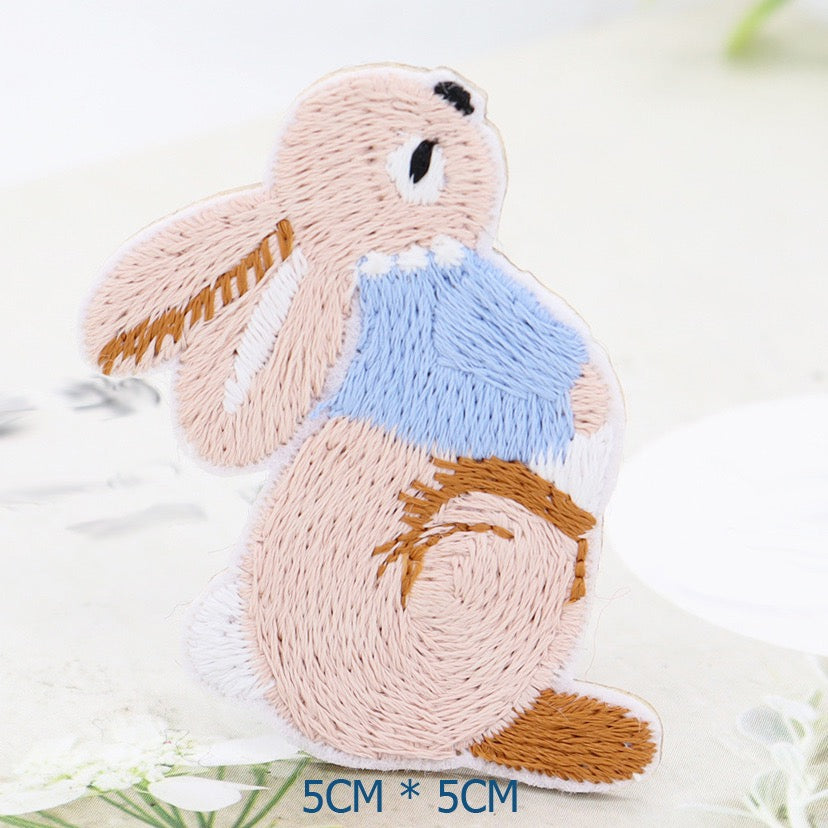 Right-facing seated bunny embroidered patch with a blue jacket and long ears trailing left

