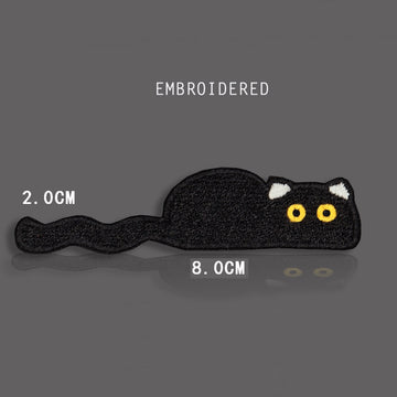 flat loafing black cat embroidered stick-on patch — fully horizontal black cat stretched 80mm wide chin on floor tail to one side with yellow eyes looking sideways