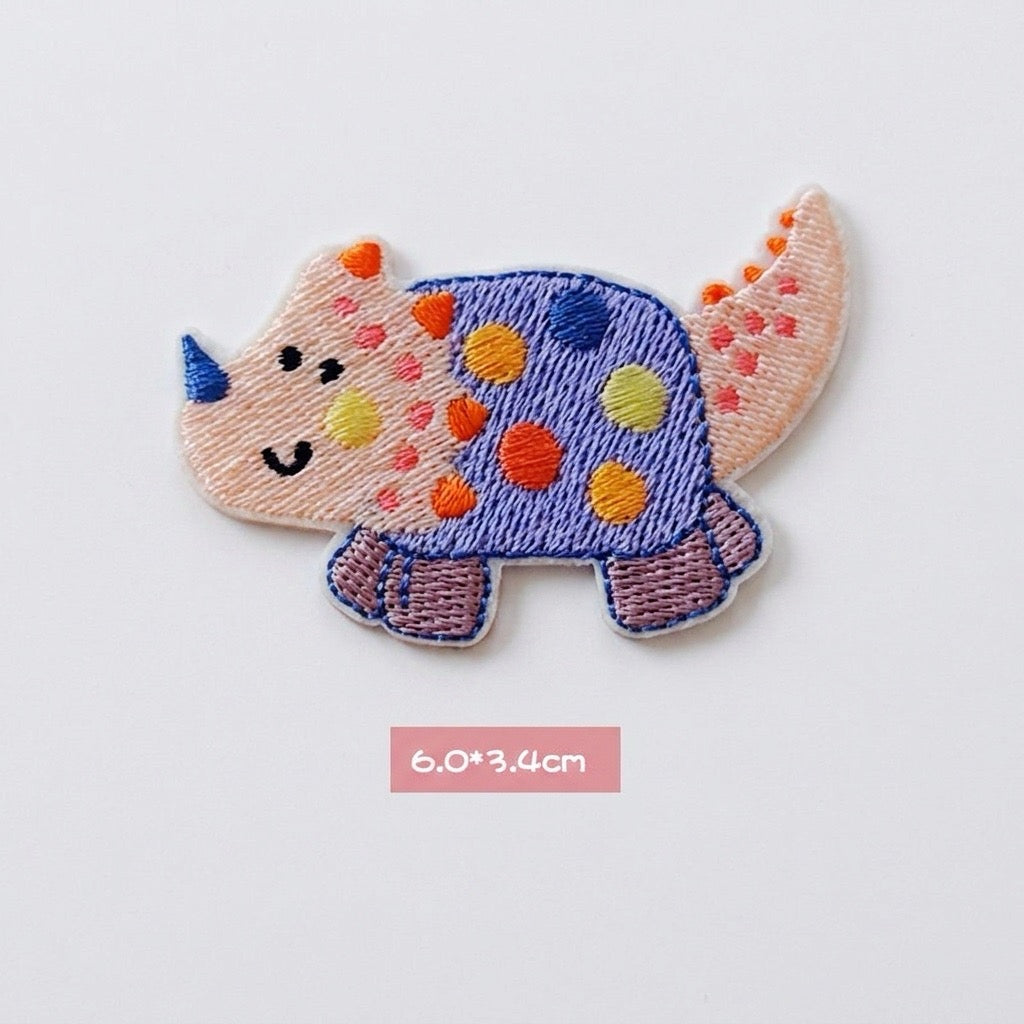 blue spotted Triceratops kawaii embroidered stick-on patch — round wide blue purple triceratops covered in large multicolored polka dots with blue horn