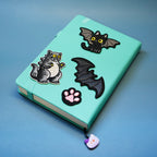 cat godzilla embroidered patch styled with other dark embroidered patches on a notebook