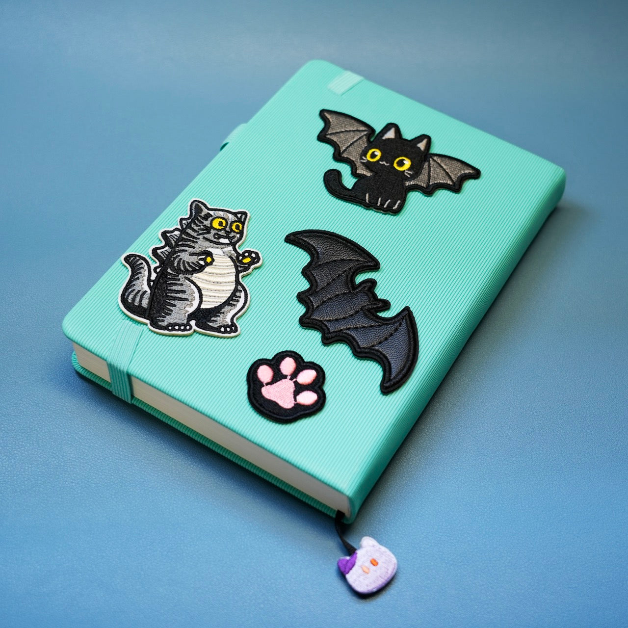 cat godzilla embroidered patch styled with other dark embroidered patches on a notebook