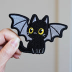 holding a large winged bat kitten embroidered stick-on patch in hand