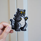 holding a cat godzilla embroidered stick-on patch in hand