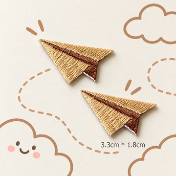 brown paper airplane embroidered stick-on patches — pair of warm golden brown satin embroidery paper planes with dark brown fold crease detail 33x18mm